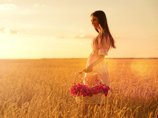 麦畑で花のかごを持つ女性