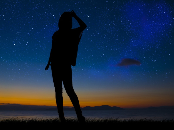 夕暮れの星空を立って眺める女性