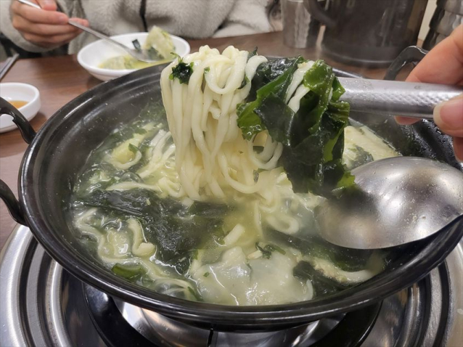 キッパルチブの海鮮ワカメうどん鍋の麺をトングですくい上げる