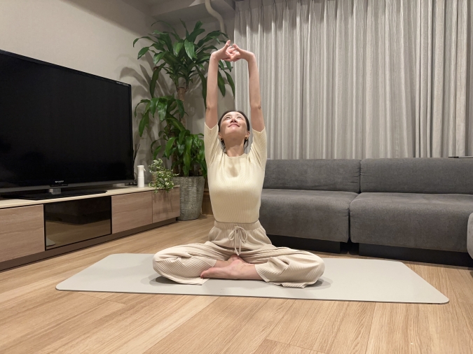 足を楽に組んで床に座り、両手を組んで大きく上に伸びる。