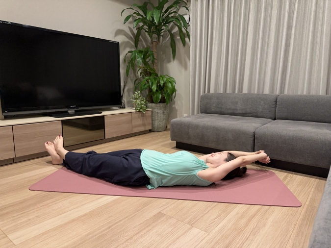 仰向けになり、両脚を肩幅に広げる。両手を頭の上にあげて背伸びをするように手の指を絡める。右手で左手首を掴み、右足の上に左足を乗せて、身体全体がゆるやかな「三日月形」になるように体側を伸ばす。